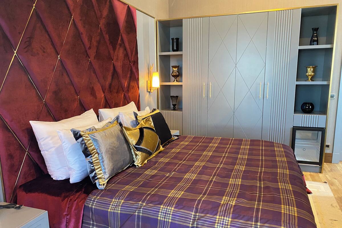 A bedroom with a large bed, a red velvet headboard, and a built-in wardrobe with shelves.
