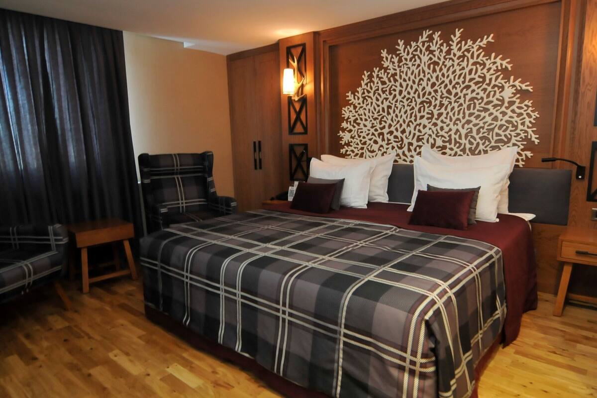 A hotel room with a large bed, a wooden headboard, a nightstand, a chair, and a wooden floor.
