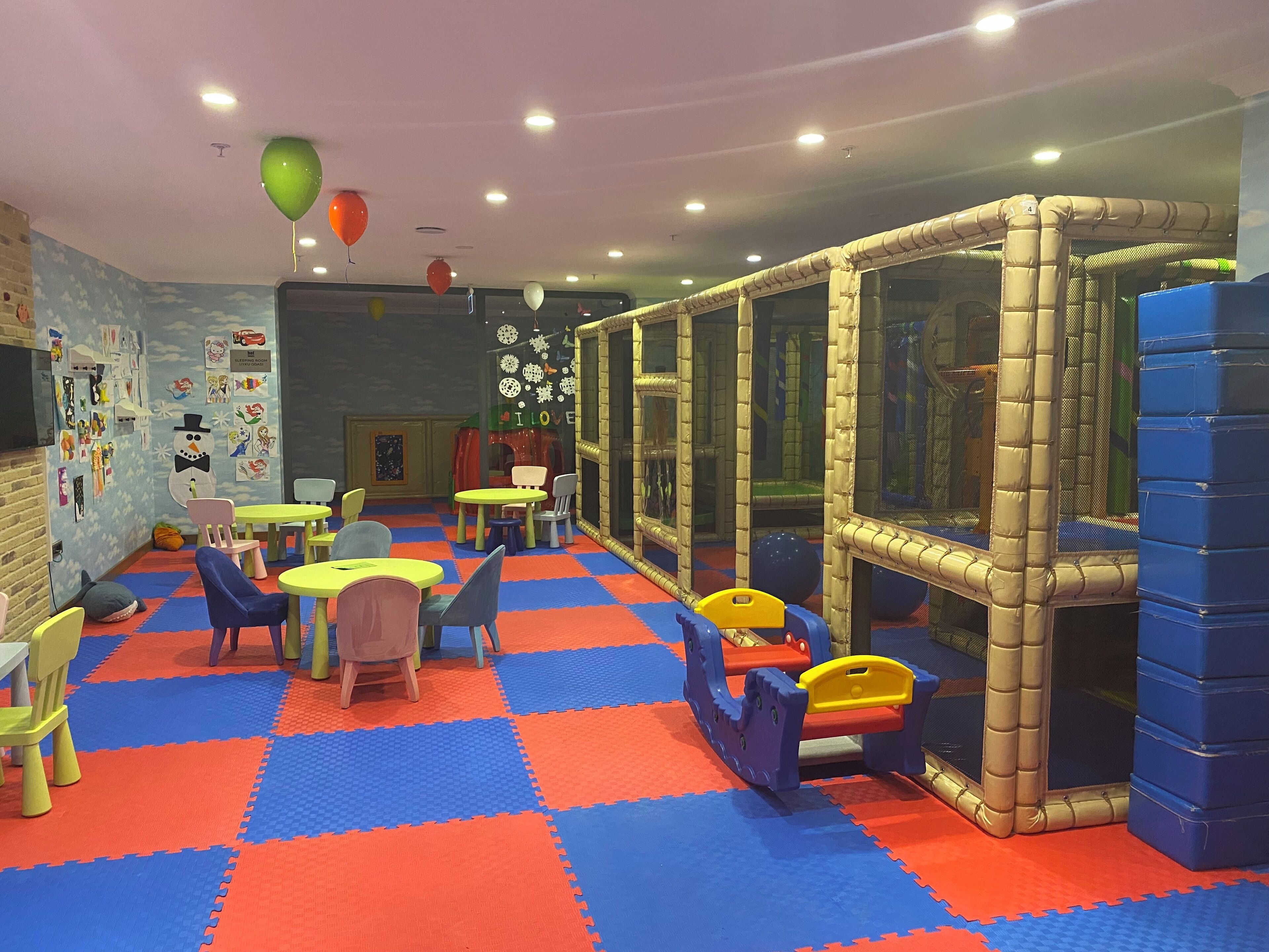 A children's play area with padded flooring, play tables, chairs, and a padded play structure.