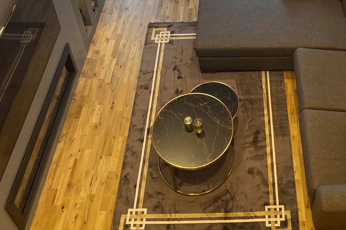 A modern living room with a wooden floor, a round marble coffee table, a grey sofa, and a unique chandelier with multiple lamps.