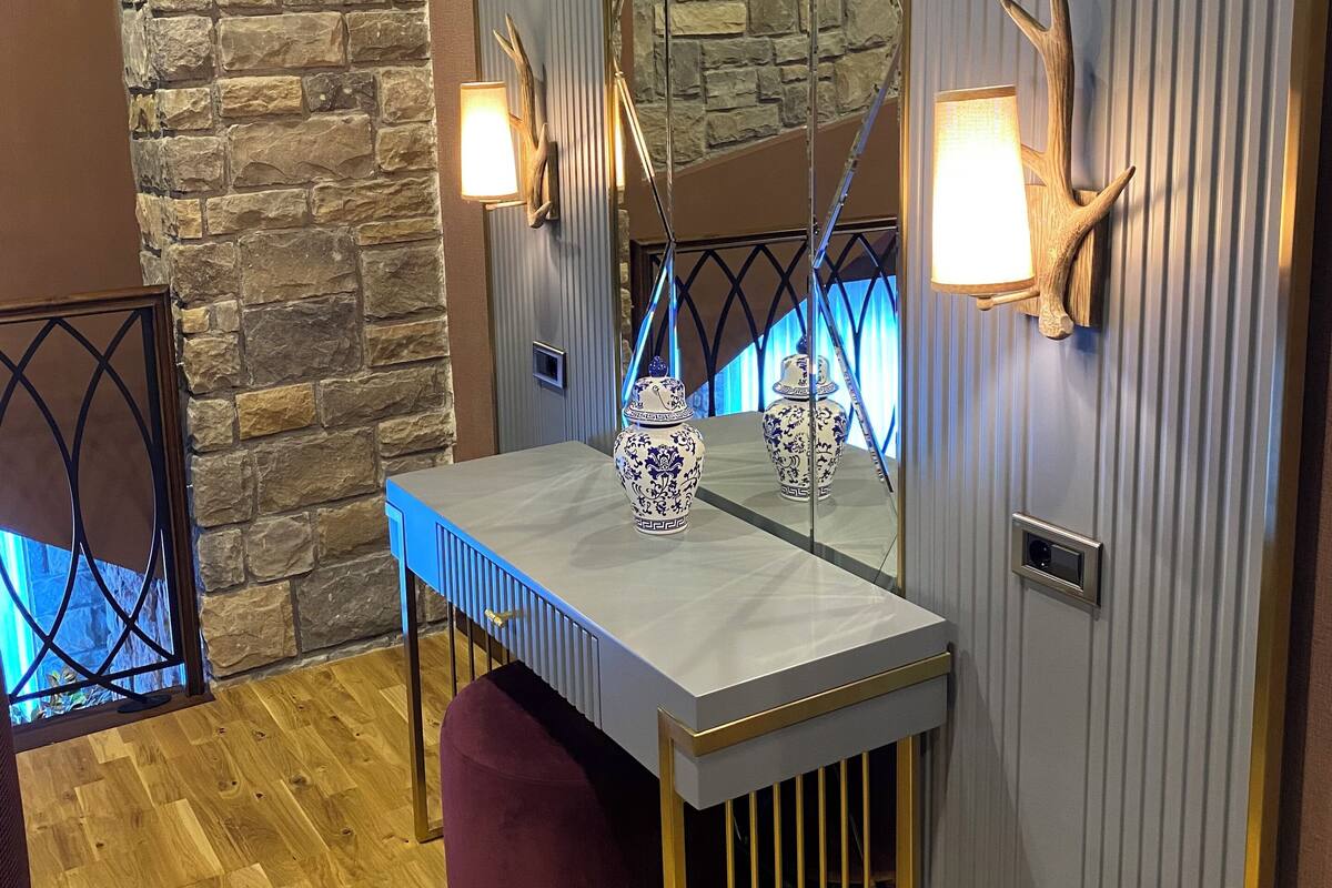 A bathroom with a stone wall, a wooden floor, a vanity with a mirror, two wall-mounted lights, and a decorative vase.