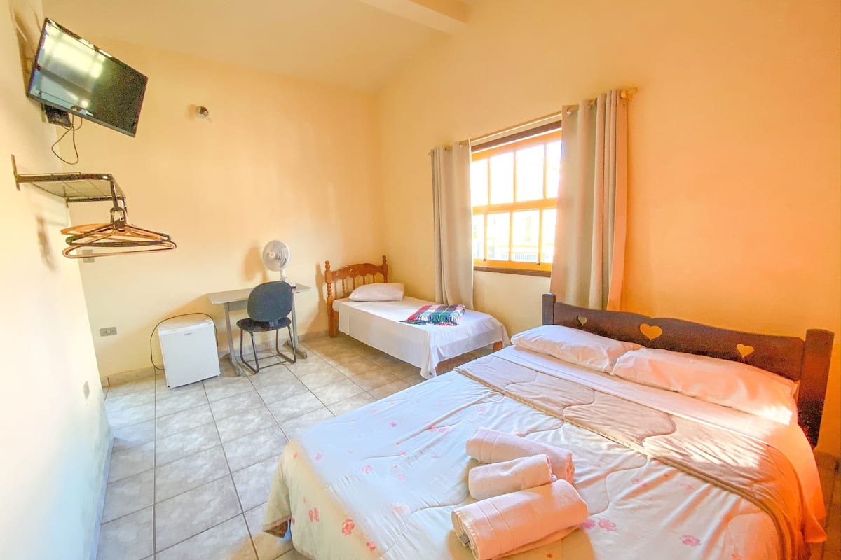A room with two beds, a desk, a chair, a TV, and a window with curtains.