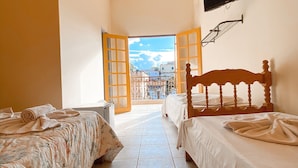 Habitación de hotel con dos camas, un televisor montado en la pared y un balcón con vistas a edificios.