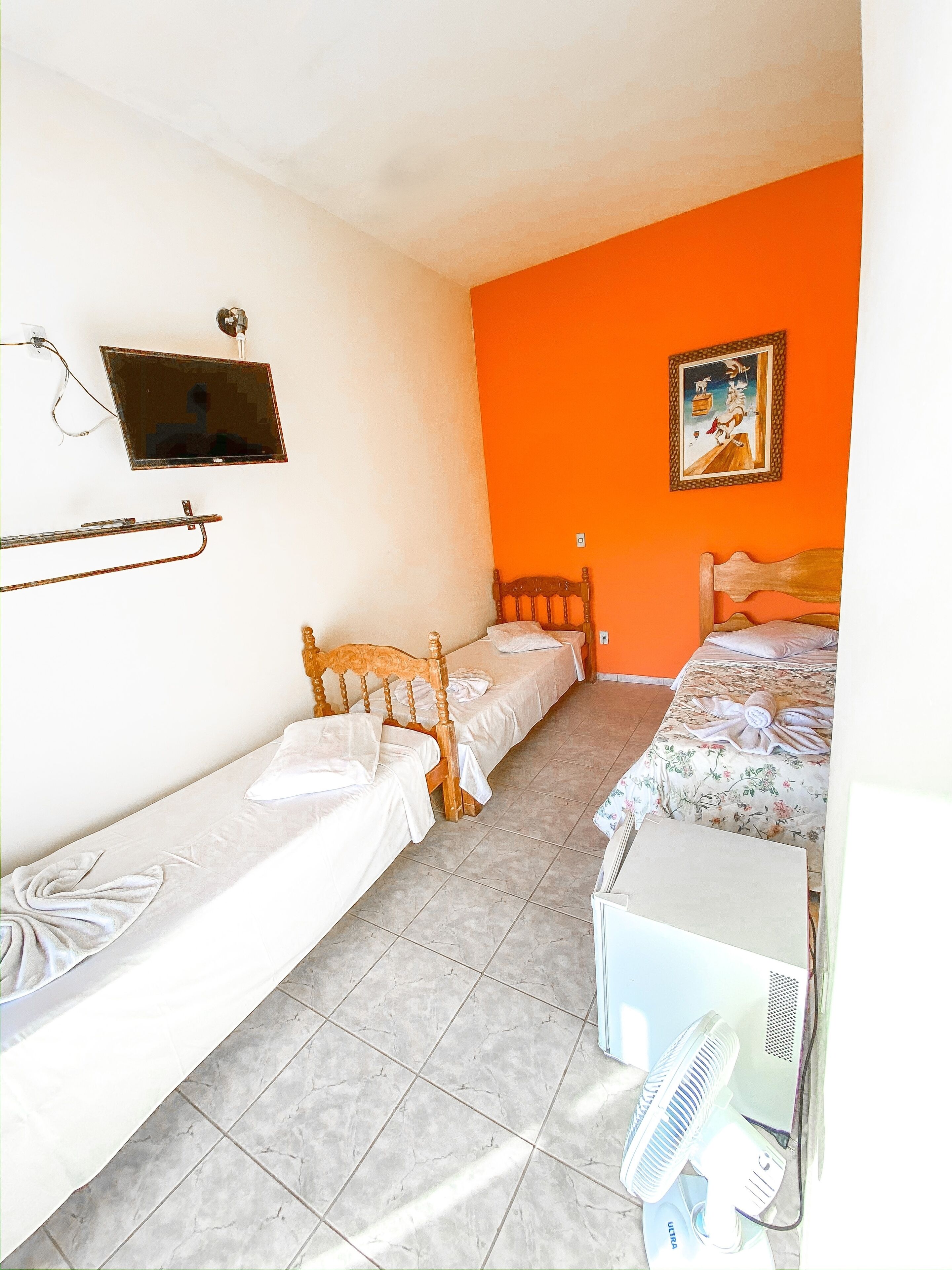 Habitació amb dos llits individuals, un panell de fusta al capçal, una taula petita, un ventilador i un quadre a la paret.