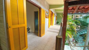 Un pasillo con puertas amarillas que dan a habitaciones, una escalera y vista a un jardín.