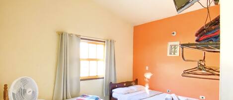 A hotel room with two beds, a desk with a fan, a window with curtains, and a wall-mounted TV.