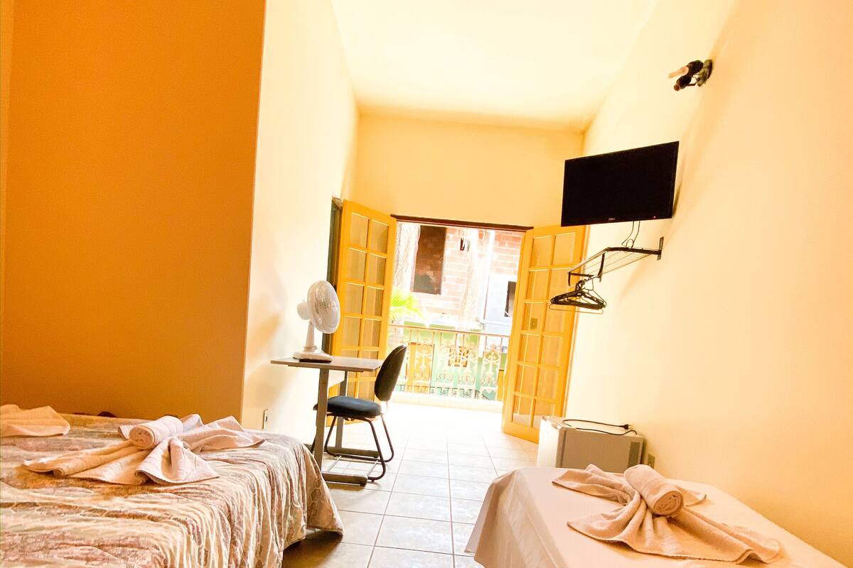 A hotel room with two beds, a desk, a chair, a TV mounted on the wall, and a window with a view of the outside.