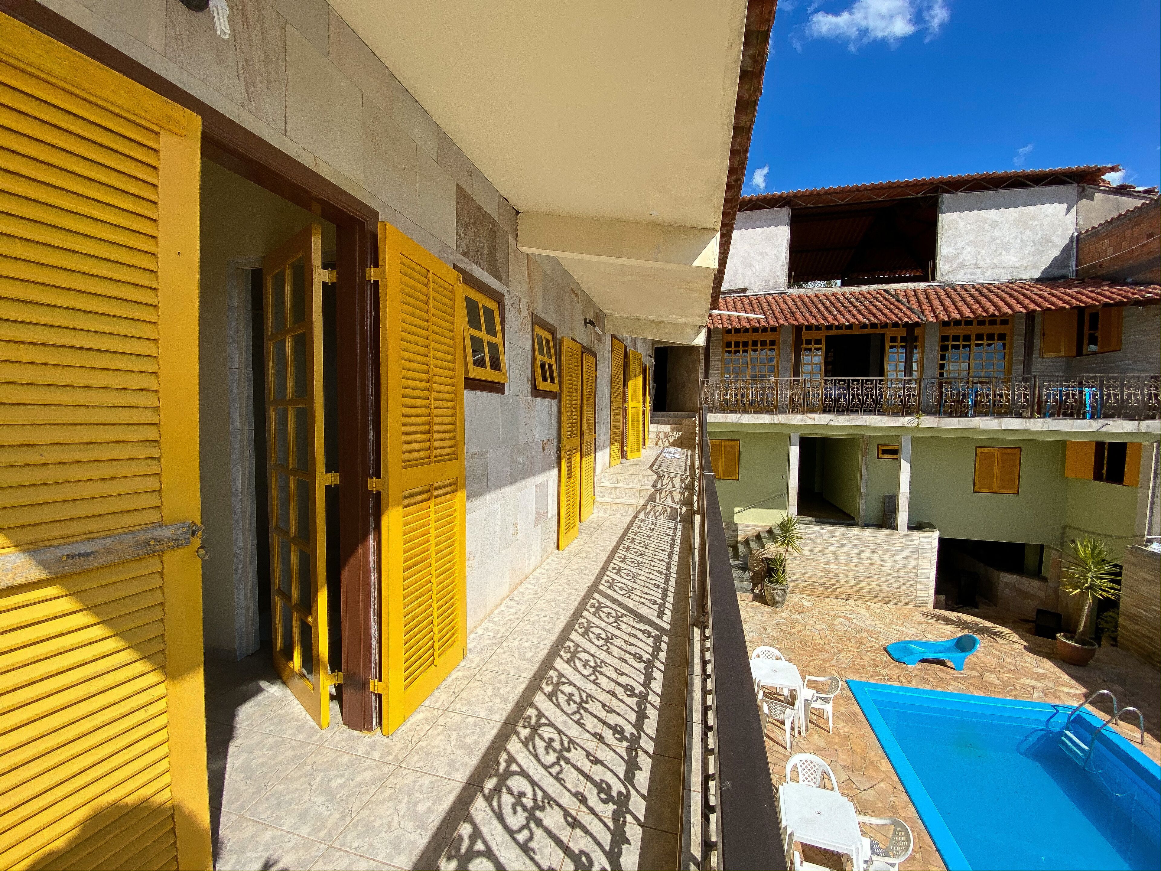 Un hotel con persianas amarillas, piscina y balcón con barandilla.