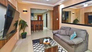 A modern living room with a sofa, a coffee table, a TV, and a dining area in the background. - Rio Spot Apartment D038 (Rio de Janeiro)