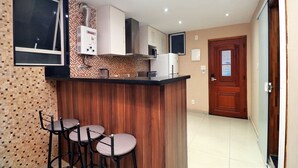 A kitchen with a wooden bar counter, three stools, a microwave, and a refrigerator. - Rio Spot Apartment D038 (Rio de Janeiro)
