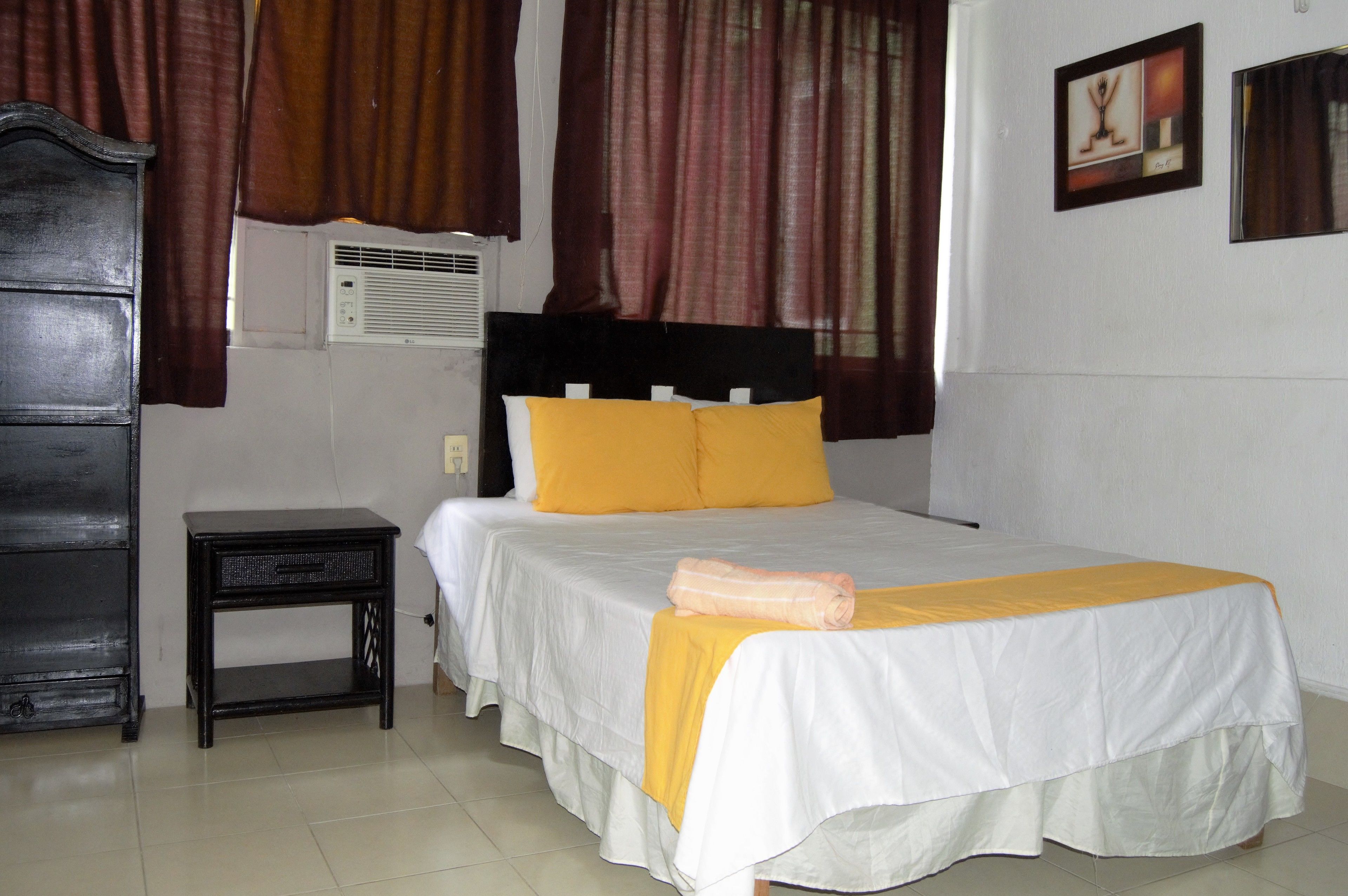 A hotel room with a bed, a nightstand, a wardrobe, and an air conditioning unit.
