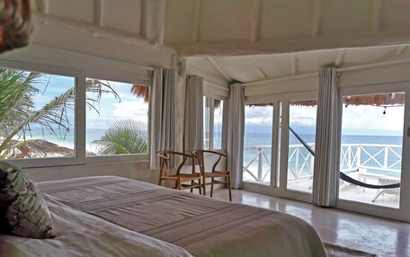 A bedroom with a large bed, a chair, and a view of the ocean through large windows.