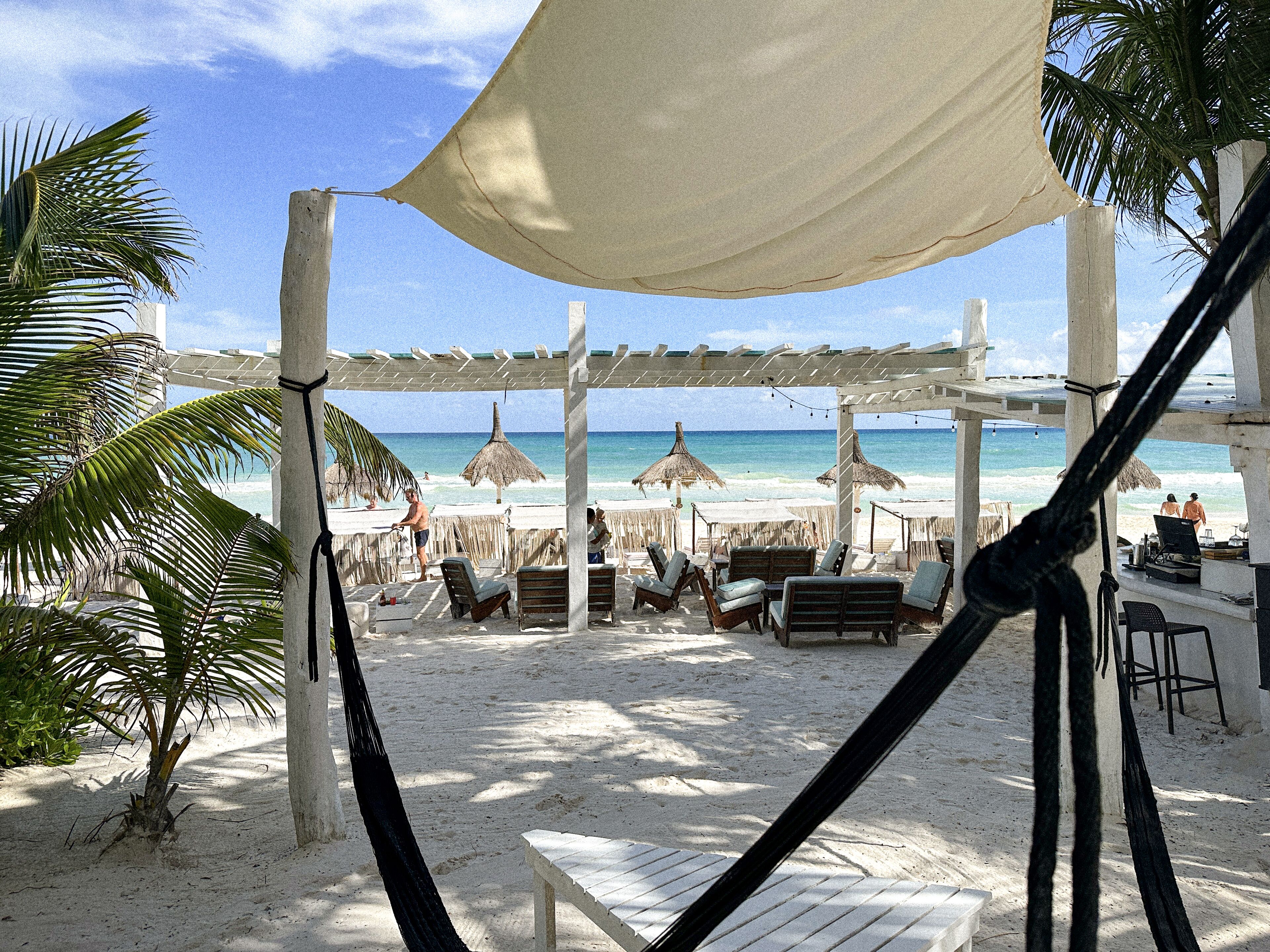A beachside lounge with thatched umbrellas, lounge chairs, and a canopy.