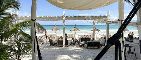 A beachside lounge with thatched umbrellas, lounge chairs, and a canopy.