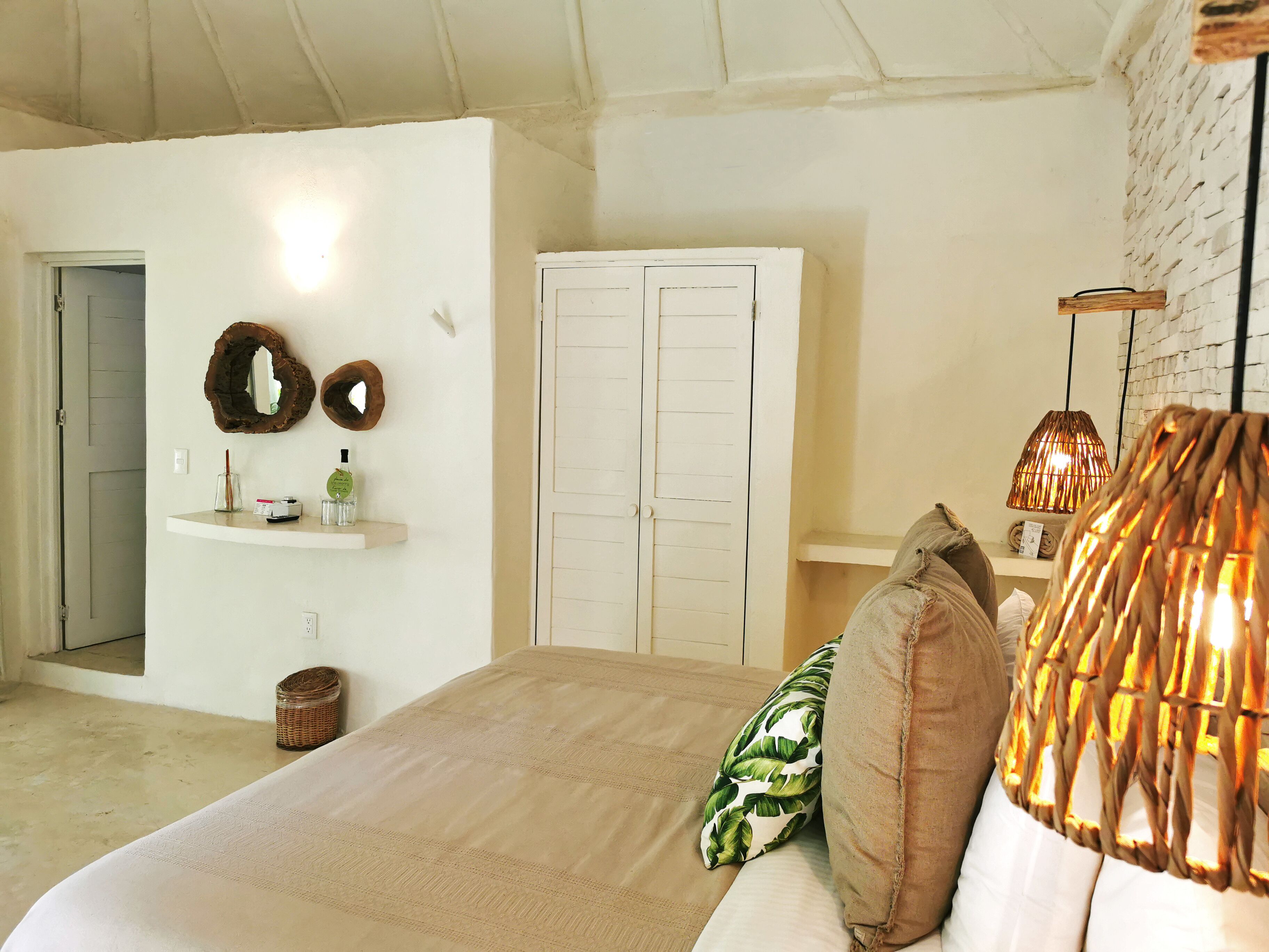 A bedroom with a bed, a wardrobe, a mirror, a shelf with toiletries, and a hanging lamp.