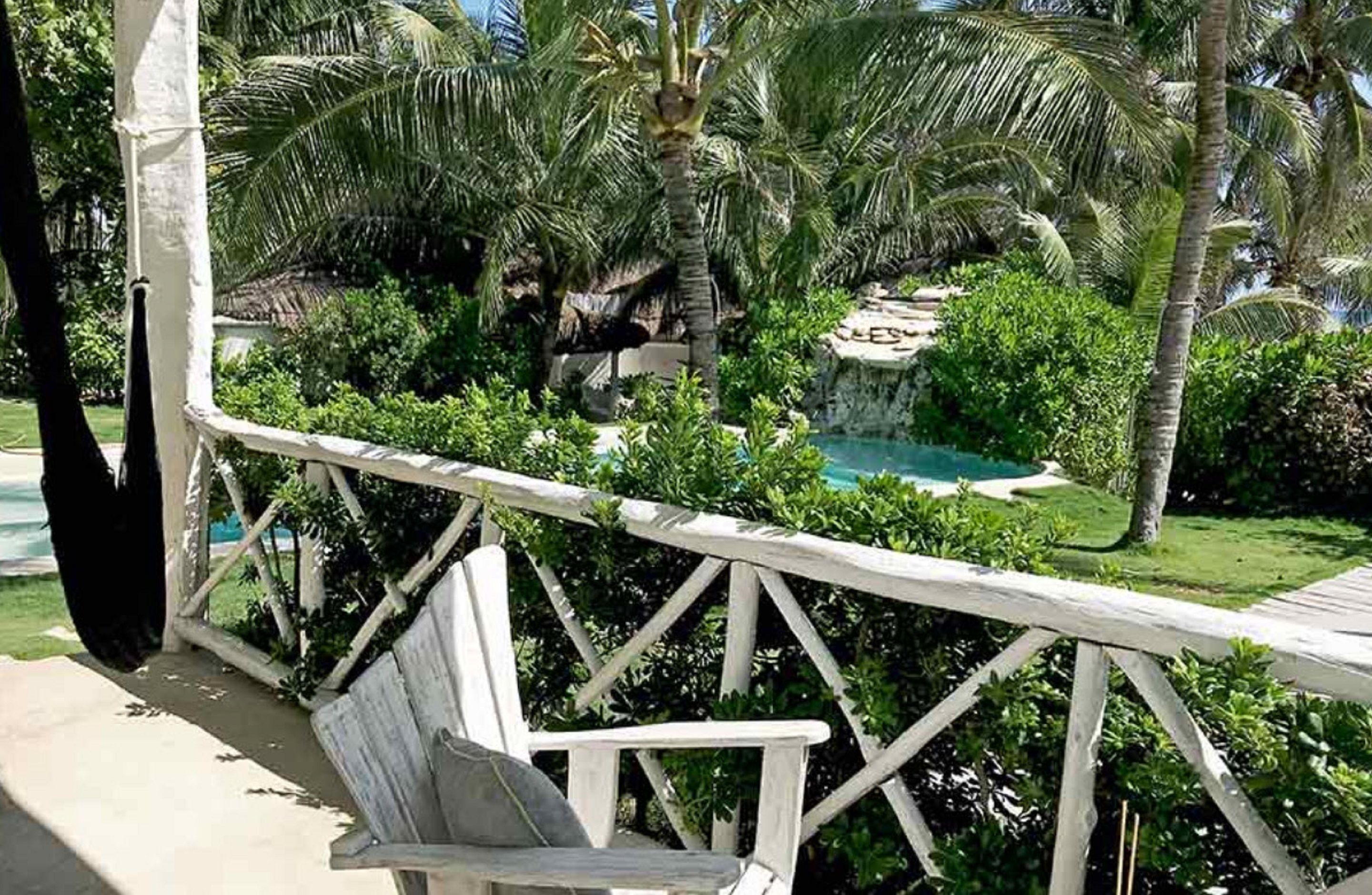 A wooden deck with a white railing overlooking a pool and lush greenery.