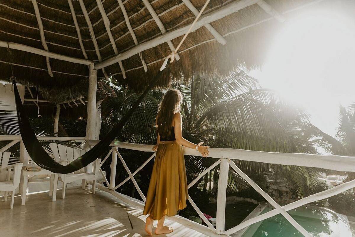 Una persona de pie en un balcón con una hamaca, con vista a una piscina y palmeras.