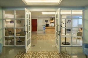 A hotel reception area with a reception desk, chairs, and a patterned carpet. - Yan's House Hotel (Kuta)