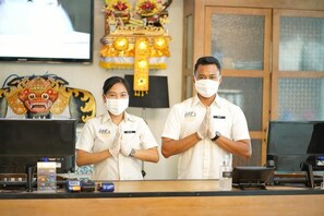 A reception desk with two staff members, a television, and a decorative altar in the background. - Yan's House Hotel (Kuta)