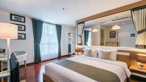 A hotel room with a large bed, a desk with a chair, a mirror, and a window with curtains. - Yans House Hotel Bali (Kuta)