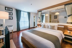 A hotel room with a large bed, a desk with a chair, a mirror, and a window with curtains. - Yans House Hotel Bali (Kuta)