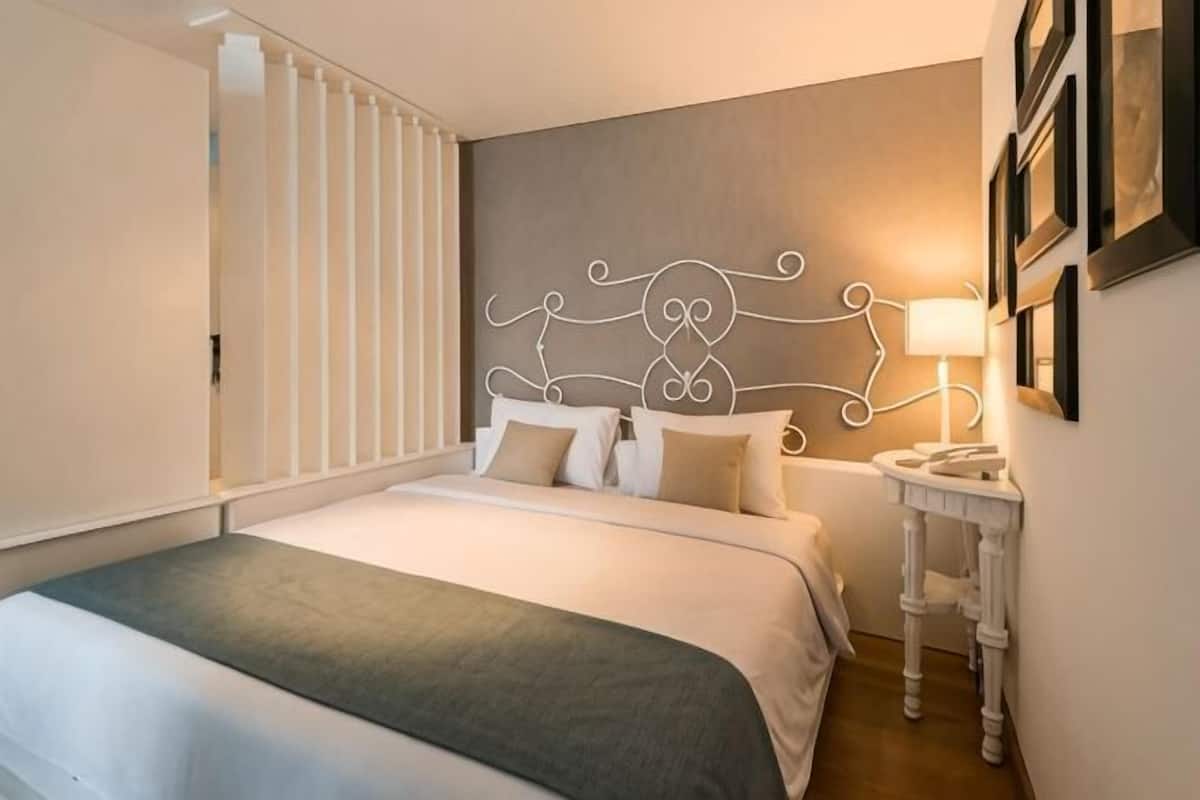Una habitación de hotel ordenada con cama, mesita de noche y decoración en la pared.