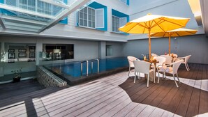 A poolside area with a wooden deck, a table with chairs, and a yellow umbrella. - Yans House Hotel Bali (Kuta)