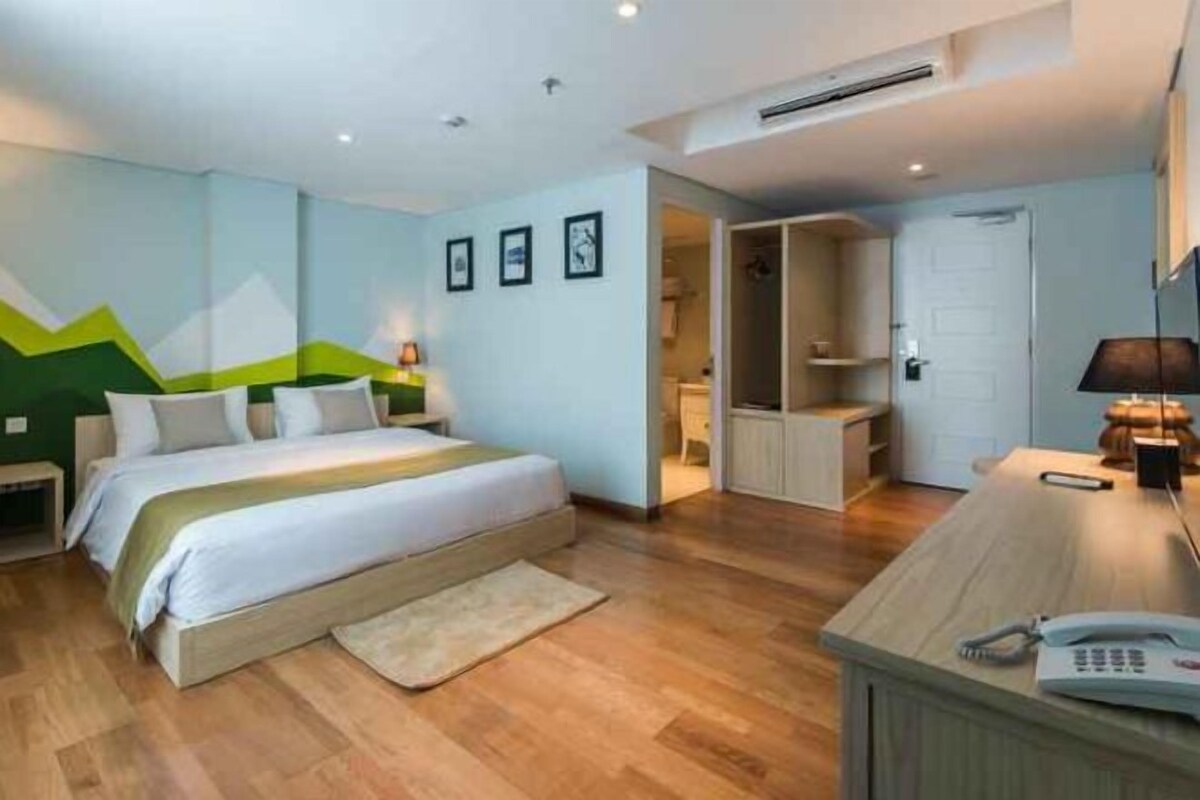 A bedroom with a bed, bedside table, lamp, and a desk with a phone.