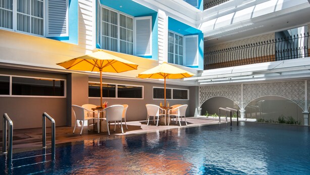 An indoor swimming pool with a sunlit terrace area, white outdoor furniture, and a view of the upper floors. - Yans House Hotel Bali (Kuta)