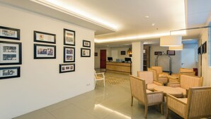 A hotel lobby with framed photographs on the walls, a reception desk, and seating area with chairs. - Yans House Hotel Bali (Kuta)
