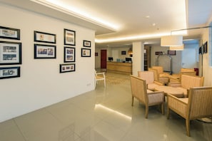 A hotel lobby with framed photographs on the walls, a reception desk, and seating area with chairs. - Yans House Hotel Bali (Kuta)