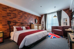 A modern hotel room with a brick accent wall, a large bed with white bedding and red accents, a red sofa, a small desk with a telephone, and a bookshelf. - Yans House Hotel Bali (Kuta)