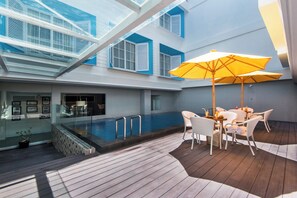 A poolside area with a table and chairs, a yellow umbrella, and a glass balustrade overlooking a swimming pool. - Yans House Hotel Bali (Kuta)