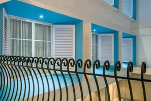 A pool area with a black metal railing, white shutters on windows, and a blue accent wall. - Yan's House Hotel (Kuta)