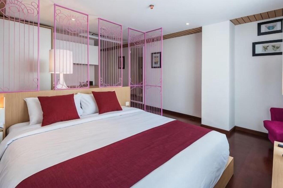 A hotel room with a large bed, a desk, a chair, and a decorative partition.