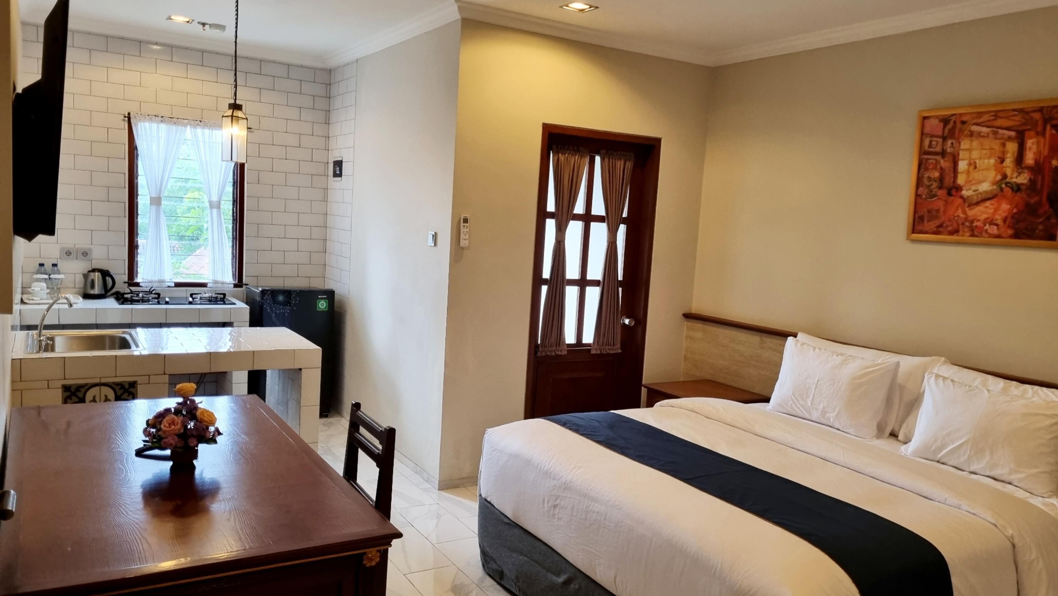 A hotel room with a bed, a desk, a kitchen area, and a door.