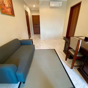 A room with a sofa, a dining table with chairs, a door, and an air conditioning unit.