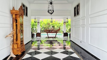 A hallway with a checkered floor, a wooden statue, and a table with a floral arrangement.