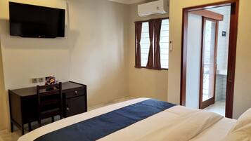 A bedroom with a bed, a desk, a TV, and a window with curtains.