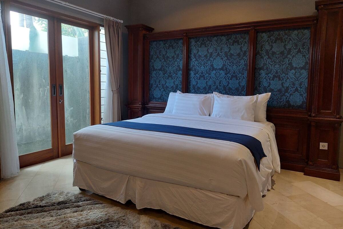 A bedroom with a large bed, wooden headboard, and a view through a sliding glass door.