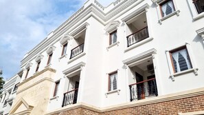 A multi-story building with white facades, multiple balconies with wrought iron railings, and a brick base. - Omatha Village (Denpasar)