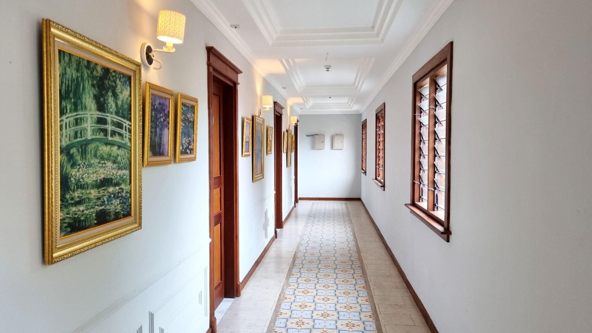 A hallway with framed artwork on the walls, a patterned floor, and a door with a wooden frame.