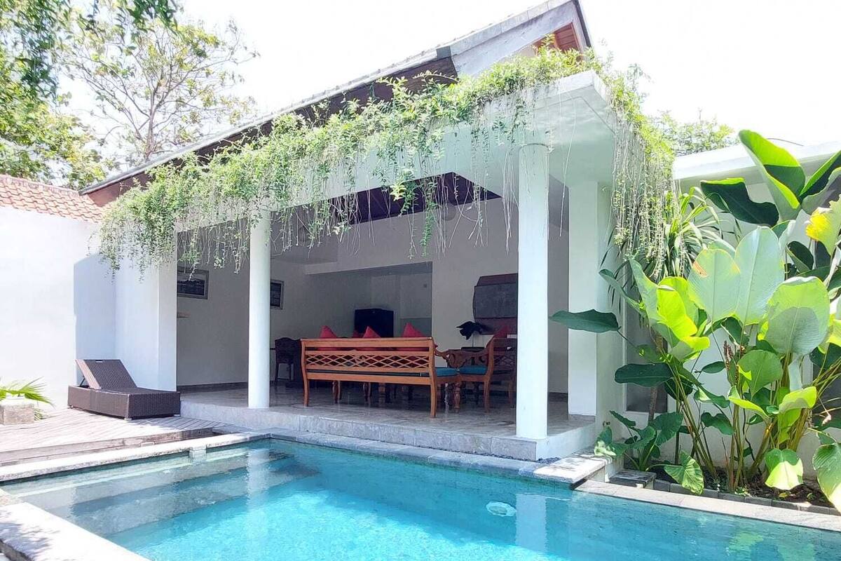 A swimming pool with a covered patio area, a table, and chairs.