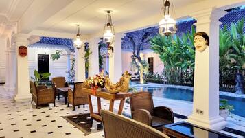 A dining area with wicker furniture, a pool, and tropical wall art.