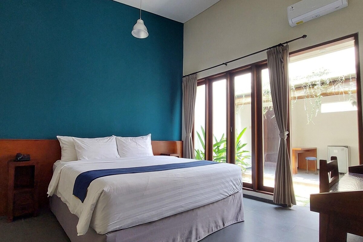 Habitación de hotel con cama, escritorio, silla, luz de techo y vistas por la ventana.
