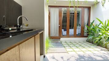 A modern kitchen with a built-in stove and sink, a wooden cabinet, and a sliding glass door leading to a patio with a tiled floor and potted plants.