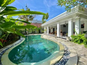 A swimming pool with a tiled edge, surrounded by a patio area with outdoor furniture and plants. - Omatha Village (Denpasar)