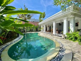 A swimming pool with a tiled edge, surrounded by a patio area with outdoor furniture and plants.