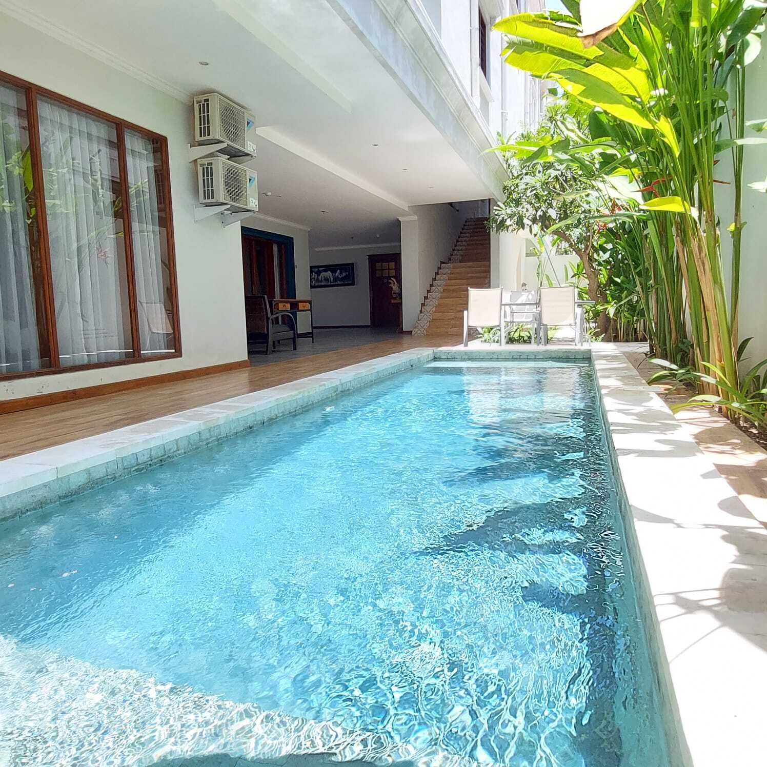 A swimming pool with a wooden deck, a staircase, and a dining area with chairs.