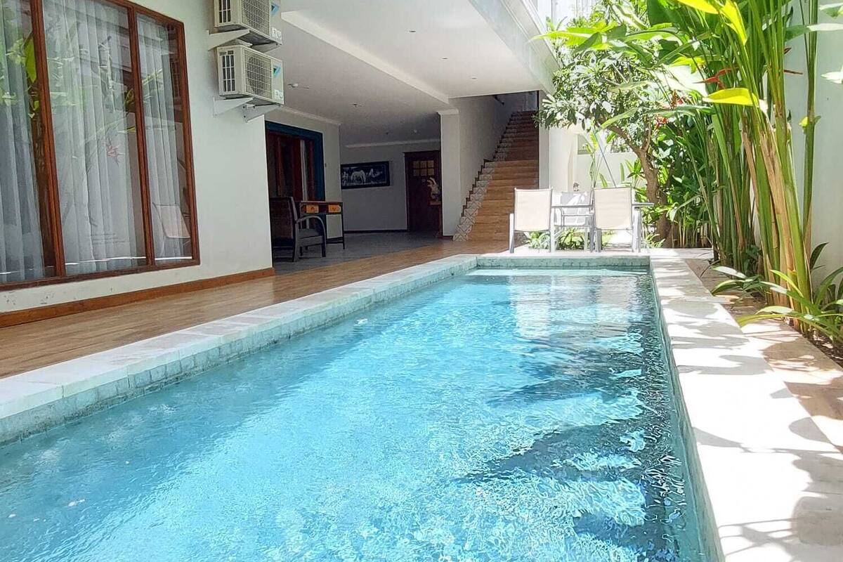 Ein Schwimmbecken mit Holzterrasse, einer Treppe und einem Essbereich mit Stühlen.